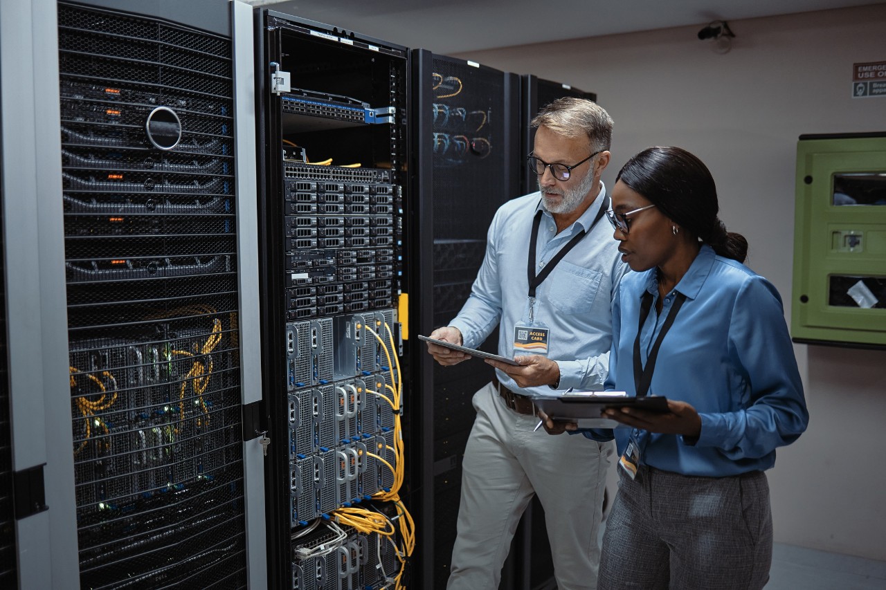 1411009466 IT technicians using a digital tablet in a server room. Programmers fixing a computer system and network while doing maintenance in a datacenter. Engineers updating security software on a machine